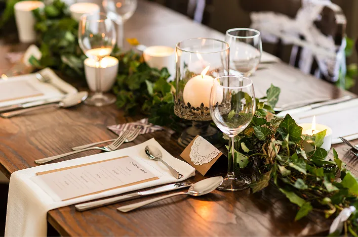 Elegant dinner table with candles, glassware, menu cards, and lush greenery garland down the center