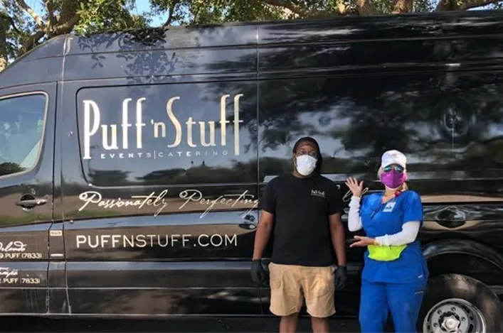 Team member and healthcare worker wearing masks stand proudly in front of a Puff ’n Stuff catering van, showing community support