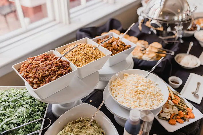 Buffet display with toppings and sides arranged in white bowls and platters, ready for guests to serve
