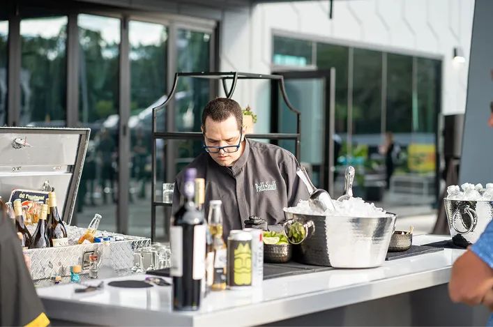 Outdoor bar setup with a Puff 'n Stuff bartender, ice buckets, lime garnish, and assorted alcohol bottles displayed.