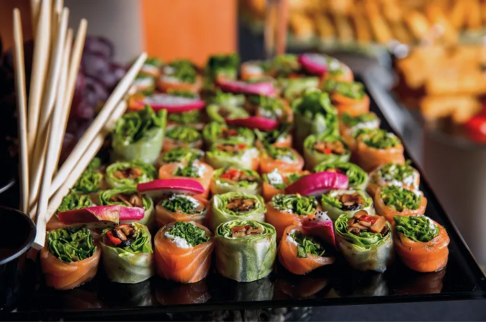 Colorful smoked salmon and veggie roll appetizers are neatly arranged on a platter with chopsticks for serving