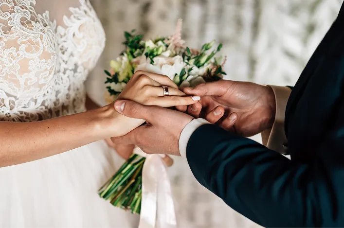 Close-up of bride and groom exchanging rings during their wedding ceremony, with bouquet and lace dress details