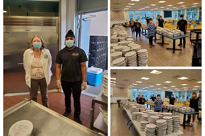 People prepare and assemble stacks of packaged food containers in a kitchen and dining area for a large event or service