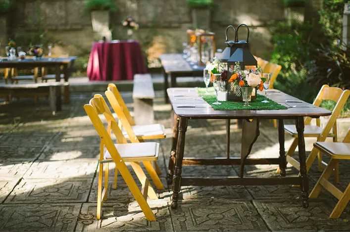 Outdoor reception table with lantern centerpiece, fresh flowers, and wooden chairs in a garden courtyard