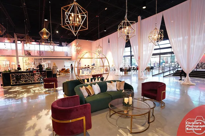 Cozy lounge setup with velvet chairs, a green sofa, gold accents, geometric chandeliers, and sheer draped curtains
