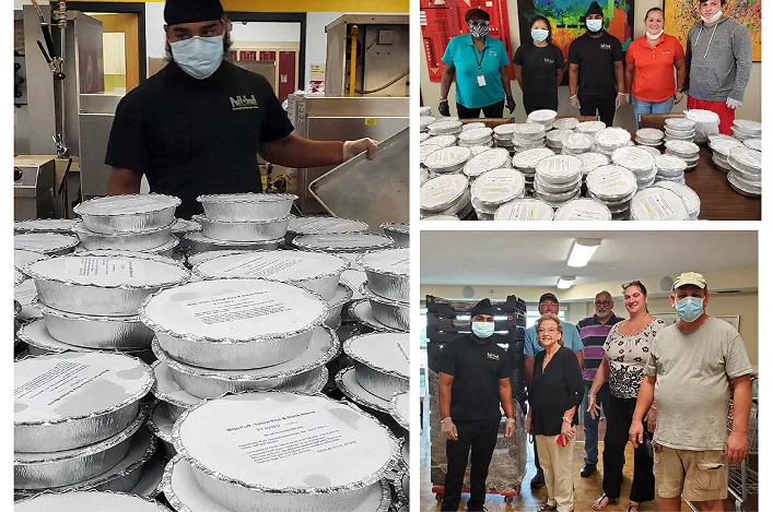 Team members wearing masks, preparing and delivering stacks of packaged meals, gathered together in a kitchen and community space