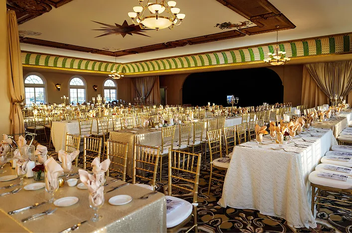 Elegant banquet hall with long tables, gold chairs, soft draped curtains, and warm lighting set for a formal event