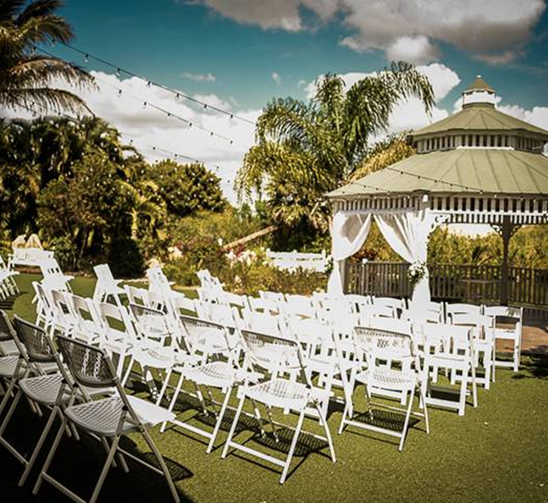 Outdoor ceremony setup at Mixon Fruit Farms with white chairs and a lush tropical background