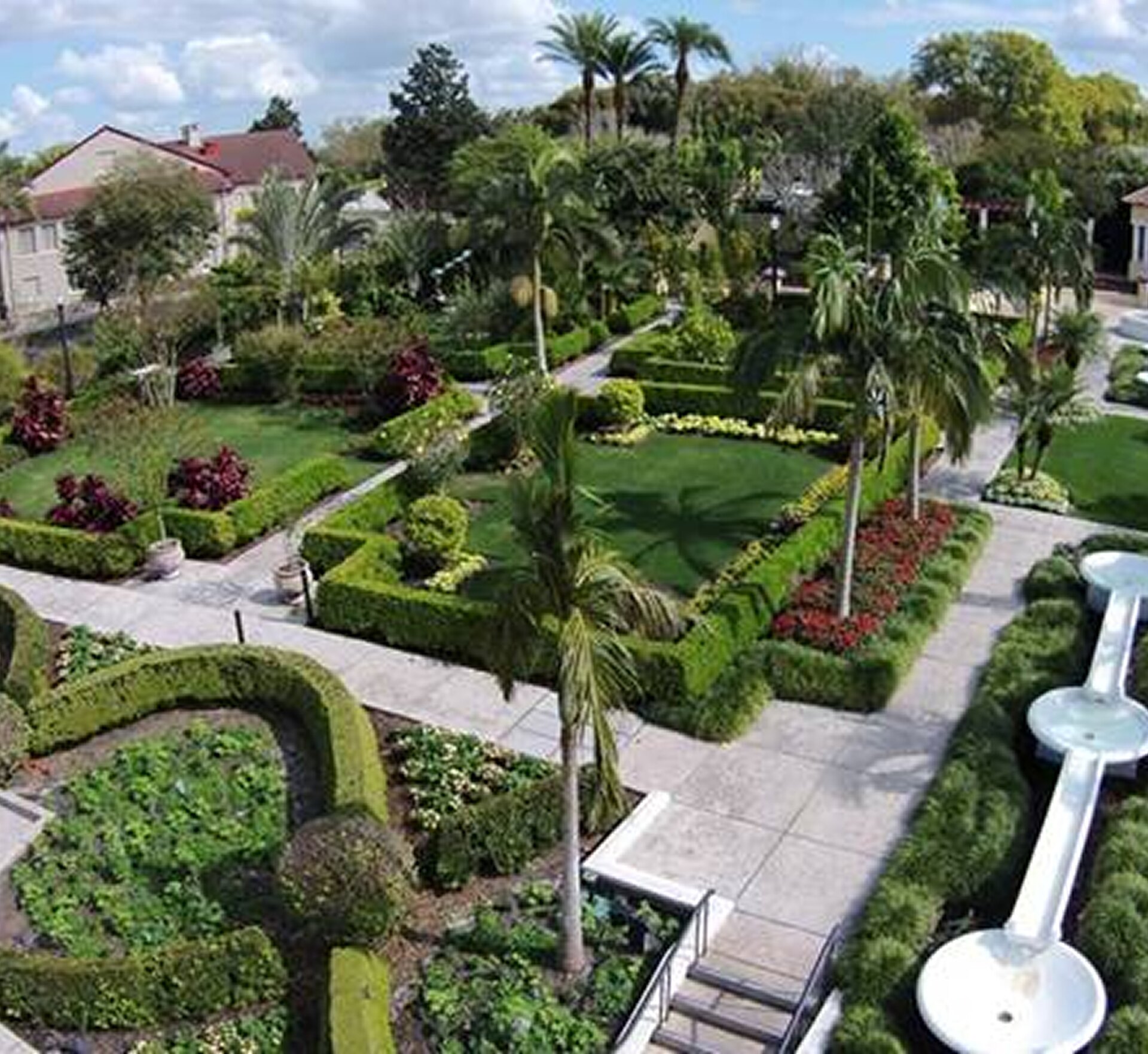 Lush garden walkways at Hollis Garden, featuring trimmed hedges, palm trees, colorful flowers and a decorative fountain